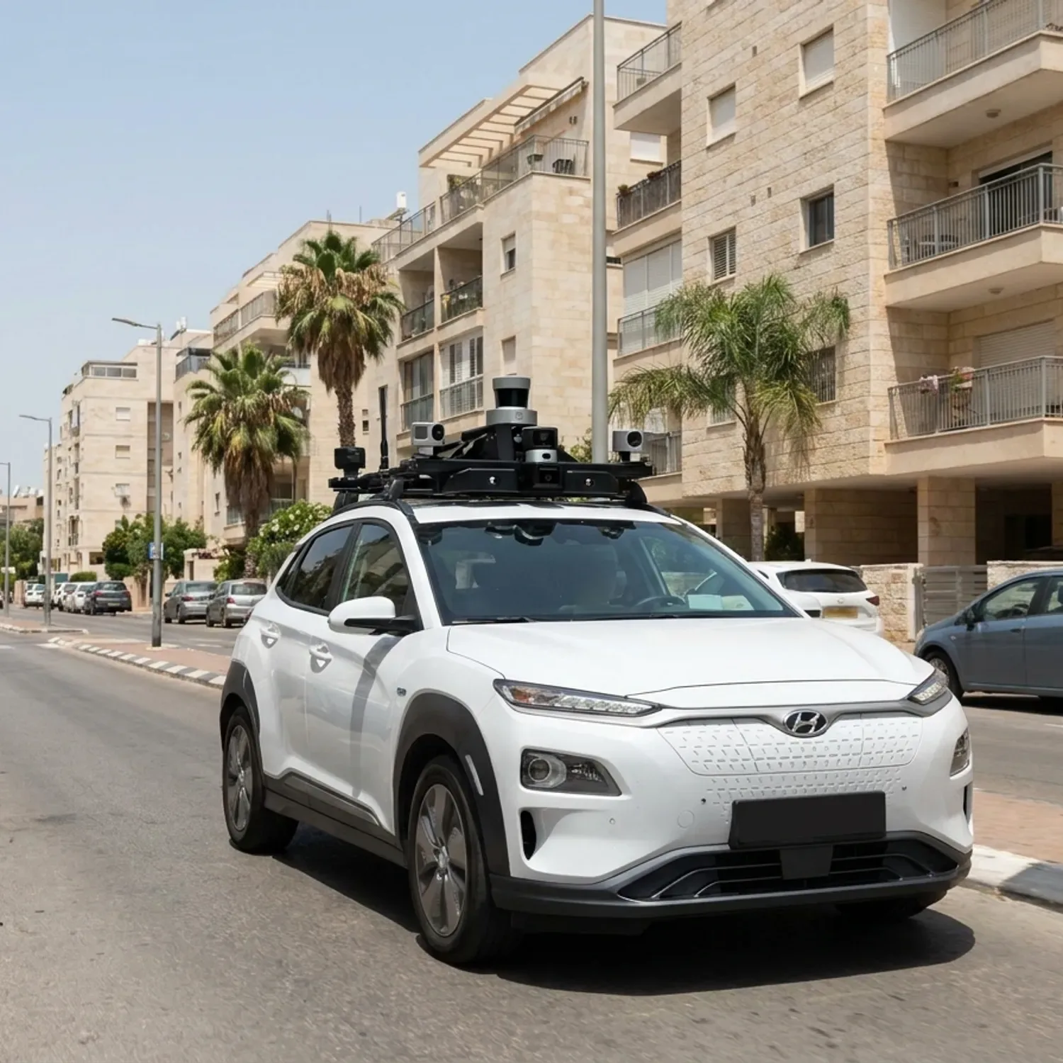 צילום חוץ מציאותי באור יום של רכב ניסוי לבן מודרני עם מערך חיישנים ומצלמות שחורות קטנות המותקנות על הגג, נוסע ברחוב עירוני ישראלי טיפוסי עם בנייני מגורים ברקע, ללא כל טקסט או לוגו על הרכב והשלטים, מראה טבעי וחד